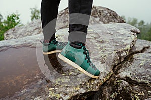 Legs of a hiker man in green boots standing on a rock in the mountains. Close photo