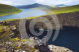 Legs of hiker sitting on top of a cliff over lake Sorvagsvatn on Faroe Islands