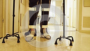 Legs of invalid in orthosis walking with support of two walking cane