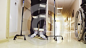 Legs of invalid in orthosis walking with support of two walking cane