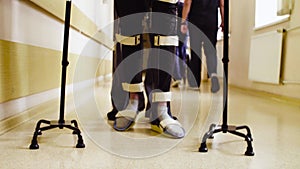 Legs of invalid in orthosis walking with support of two walking cane