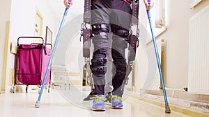 Legs of invalid in robotic exoskeleton walking through the corridor