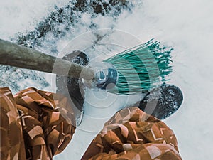 Legs of a janitor and a broom in the winter snowy season. View from top to bottom on the pavement.