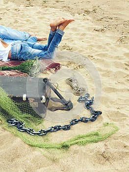 Legs in jeans, men and women lying on a plaid blanket on the sand on the beach with a valise