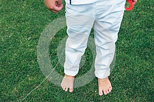 Legs of little boy in white jeans. Boy is standing on the grass. Child`s bare feet.