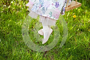 Legs of little girl on swing. Nature on background. Childhood. Summer