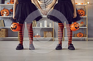 Legs of little girls in Halloween costumes standing holding hands in room with festive decor.