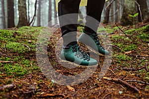 Legs of a male tourist in green boots standing in the woods on the ground in moss, close up photo