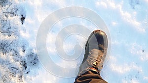 Legs of a man in black boots walking in the snow in the setting sun