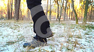 Legs of a man in black boots walking in the snow in the setting sun