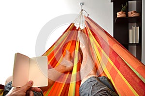 Legs of man lying down in bright hammock holding empty notice book in his hand