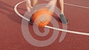 Legs of a man practicing ball skills by rolling a basketball between his legs on an outdoor court in the summer