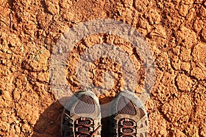 The legs of a man in sneakers a dry polluted red stony soil.