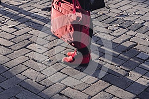 Legs of a man standing at a traffic light wearing red suede boots and a red laptop bag