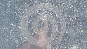 Legs of man walking under water along bottom of sea with pebbles. Male feet going on beach under water. Point of view