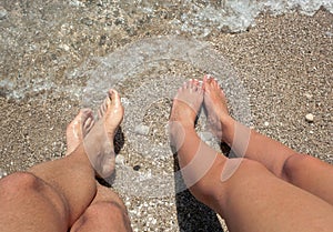 Legs of a man and a woman with her feet in the sea