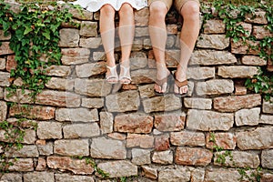 Legs of a man and a woman sitting side by side on the stone fence