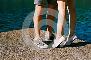 Legs of a man and a woman in sneakers standing hugging each other on the pier close-up, a woman is standing on tiptoe