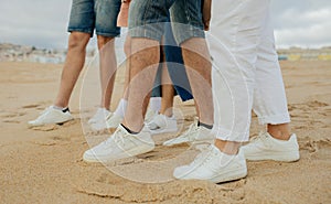 Legs of millennial diverse people in white sneakers on beach, outdoor, cropped. Active game, picnic