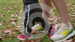 Legs of mom walking with baby in autumn park touching baby to go holding hands.