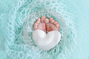 Legs newborn baby close up on a blue background with a toy in the form of a heart