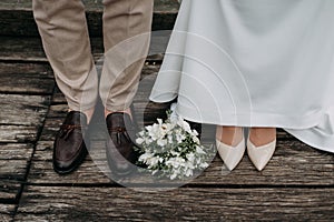 Legs of newlyweds on wooden background. stylish shoes of bride and groom outdoors. bridal bouquet on brige close up