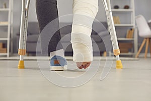 Legs part of young man with broken leg in cast walking with crutches at home