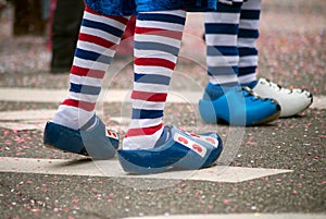 legs of people parading in the street with blue wooden shoes and striped socks