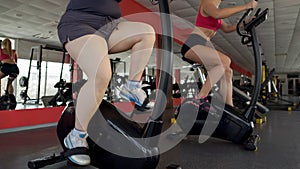 Legs of plump and slim women pedaling on stationary bikes in gym, sport workout photo