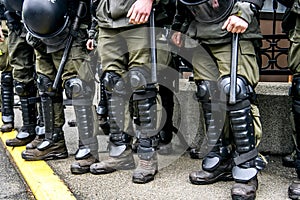 Legs of a policemen in protective ammunition and a green uniform. Knee pads, helmets, batons, boots