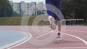 Legs in red snikers of a young woman athlete who starts running at the city athletics track during training in slow