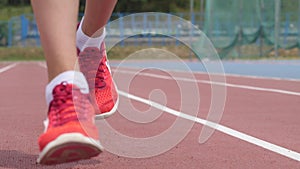 Legs in red snikers of a young woman athlete who training running at the city athletics stadium during a day training in