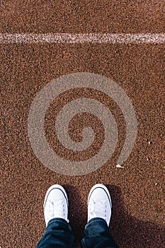 Legs on red tartan sports field with two shoes, personal perspective from above