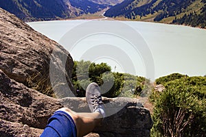 Legs resting on a mountain near calm lake water, summer day