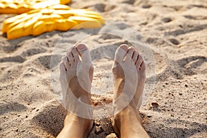 Legs on sandy beach in the summer, woman relaxing with barefeet on sandy shore