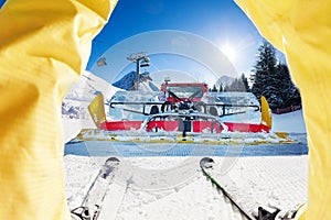 Between legs shoot of skier against snow grooming tractor