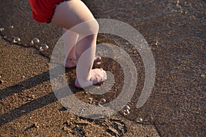 The legs of a small child on a sandy beach by the sea. A child is wetting his feet in the sea