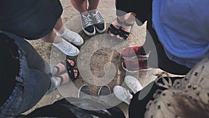 Legs and sneakers of teenage boys and girls standing in half circle on the sand.