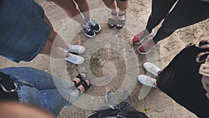 Legs and sneakers of teenage boys and girls standing in half circle on the sand.