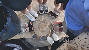 Legs and sneakers of teenage boys and girls standing in half circle on the sand.