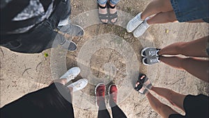 Legs and sneakers of teenage boys and girls standing in half circle on the sand.