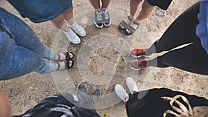 Legs and sneakers of teenage boys and girls standing in half circle on the sand.