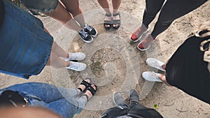 Legs and sneakers of teenage boys and girls standing in half circle on the sand.