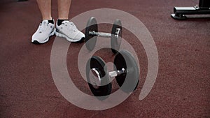 Legs of sportsman is walking near the dumbbells in gym on floor during the rest between reps.