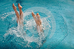 Legs of synchronized swimmers girls peeking out of the pool water in a show performance