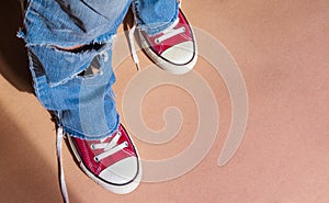 legs in tattered blue jeans and red sneakers with untied laces