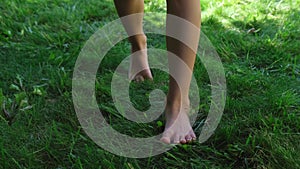 legs of a teenage girl barefoot walking towards the camera, stepping on green grass or lawn, front view