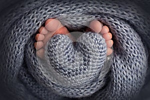 Legs, toes, feet and heels of a newborn. Wrapped in a gray knitted blanket. Knitted heart in baby& x27;s legs.