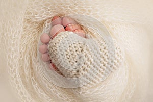 Legs, toes, feet and heels of a newborn. Wrapped in a white knitted blanket. Knitted heart in baby& x27;s legs.