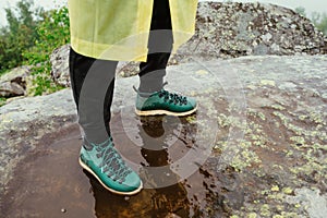 Legs of a tourist in boots in rainy weather on a rock, close photo. The tourist travels in bad weather in the mountains